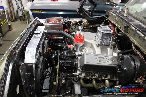 Ford V8 engine with racing valve covers and headers. Another vehicle is visible in the background