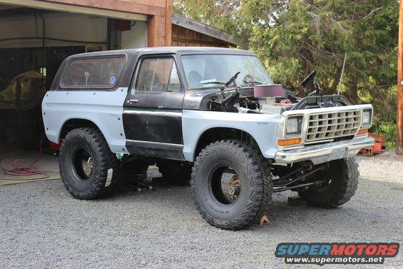 Gray and black Ford Bronco with hood open, large tires, and unfinished body panels