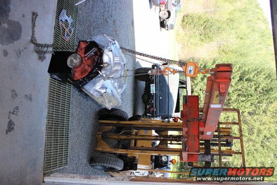 Engine and transmission assembly suspended by chains and a hoist, with a forklift preparing to move it