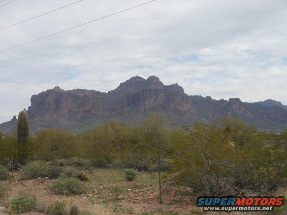 Desert scene with Superstition Mountains, a saguaro cactus, and scrub brush under a cloudy sky
