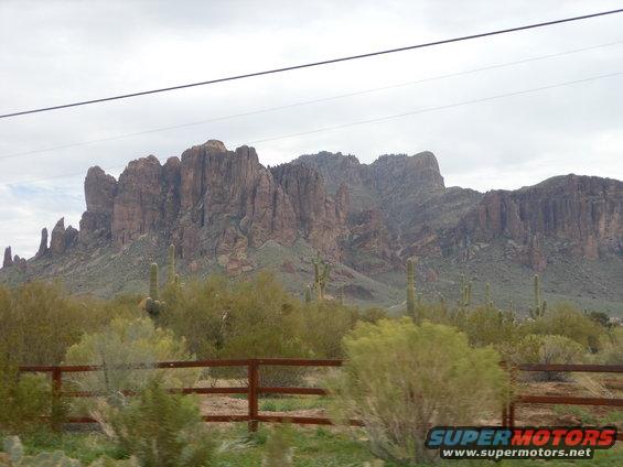 Desert mountains and saguaro cacti under a cloudy sky, with a wooden fence in the foreground