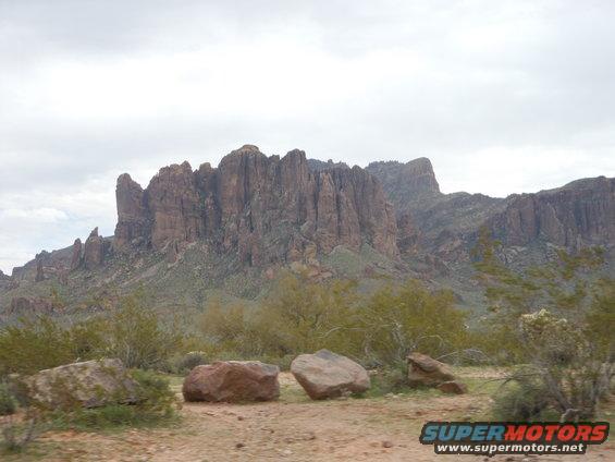 Desert mountains under a cloudy sky, with rocks and scrub brush in the foreground