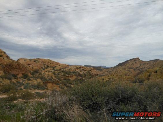 Desert landscape with rocky hills and dry brush under a cloudy sky