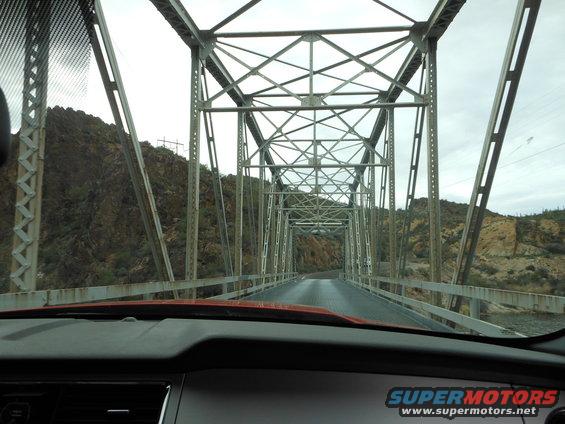 View from inside a car driving over a large metal truss bridge with rocky hills on either side