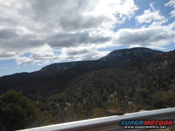 Mountain landscape with trees under a cloudy sky, seen from a vehicle