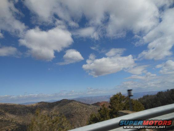 Mountainous terrain under a blue sky with scattered clouds, seen from a vehicle