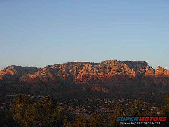 Red rock mountains illuminated by sunset, with trees and a small town in the foreground