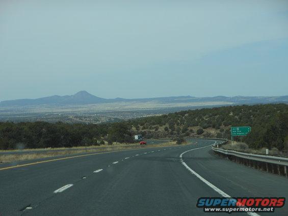 Highway curves ahead with mountains in the distance. A red car and a truck are visible on the road