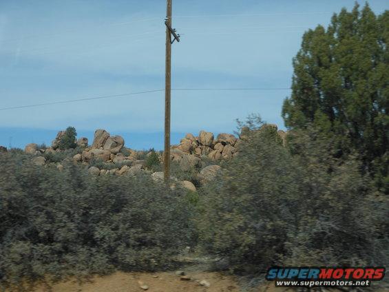Desert landscape with rocks and trees, utility pole, Supermotors logo