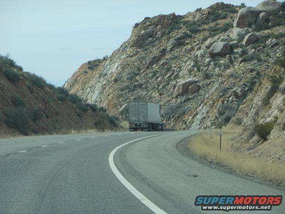 Semi-truck driving on a winding highway through a rocky, mountainous area