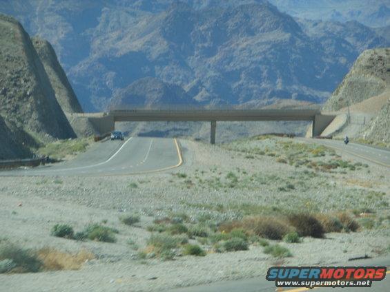 Car on highway under a bridge in a mountainous desert landscape