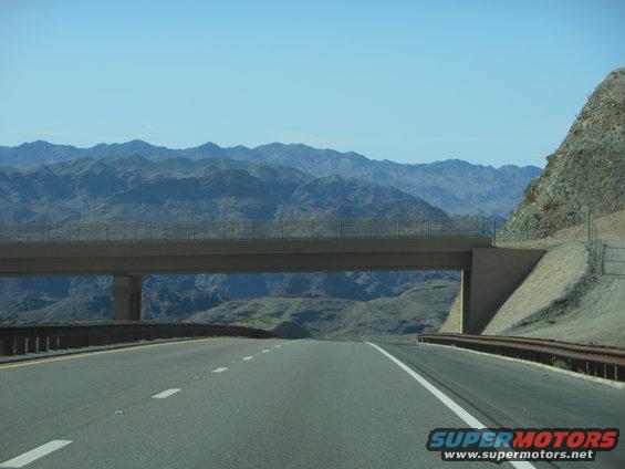 Highway overpass crossing a desert road with mountains in the background