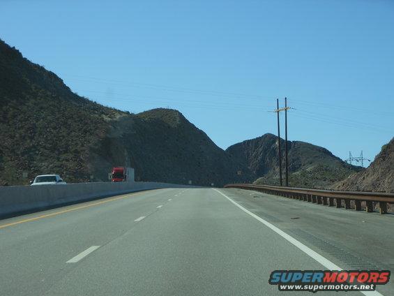 Highway driving through a mountainous desert landscape with a white car and a red semi-truck visible