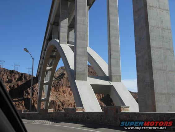 Concrete bridge arch over a road with rocky hills and power lines in the background
