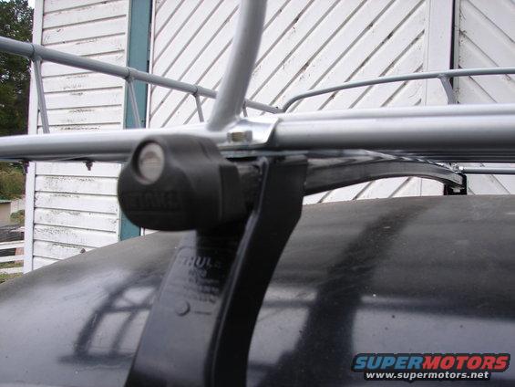 Close-up of a black Thule roof rack clamp attached to a dark car roof