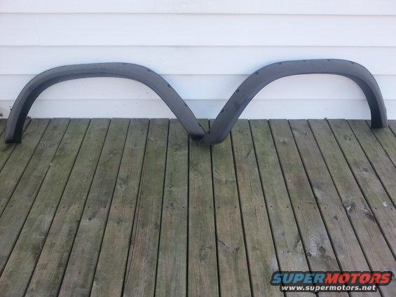 Two dark gray plastic fender flares laid on a wooden deck