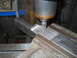 1992 Ford Bronco - A milling machine is used to cut a metal part, with metal shavings accumulating around the workpiece.