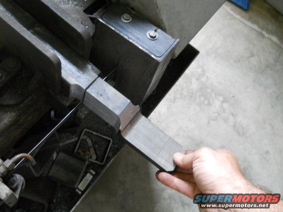 Hand holding metal piece being cut by a band saw