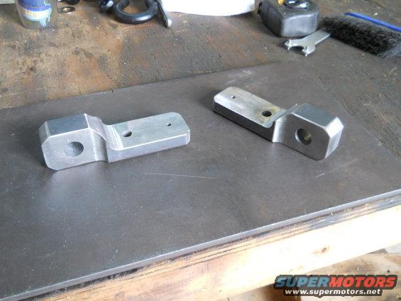 Two metal parts on a workbench, one in foreground, one in background