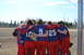 1990 Chevrolet Suburban - A team huddles together on a baseball field under a bright sky.