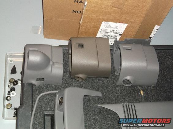 Several gray plastic steering column covers and some hardware are laid out on a gray carpeted surface. A cardboard box is in the background