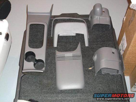 Several gray plastic interior trim pieces, including a center console section with cup holders, laid out on a gray carpeted surface
