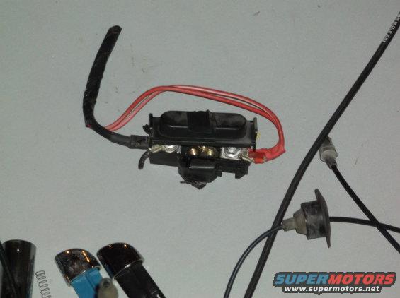 Automotive fuse box with red and black wires attached to terminals, against a light gray background