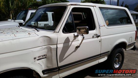 White Ford Bronco with damage to the front fender. Another white vehicle is parked behind it