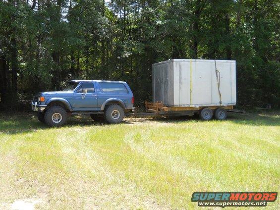 Blue 1987 Ford Bronco towing a white cargo trailer on a grassy field