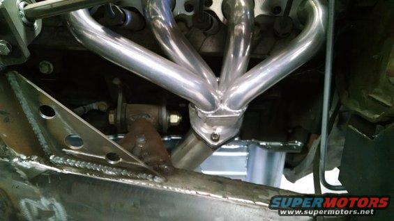 Close-up of shiny exhaust headers on an engine, with custom metal fabrication visible below
