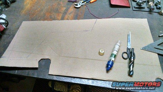 Cardboard template with cutouts and pencil lines, next to a marker, scissors, and a brass fitting