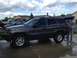 2004 Jeep Grand Cherokee - A man loads an item into the back of a parked Jeep Grand Cherokee, with other vehicles visible in the background.
