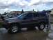 2004 Jeep Grand Cherokee - A dark gray 2004 Jeep Grand Cherokee is parked in a driveway with its rear hatch open, alongside other vehicles.