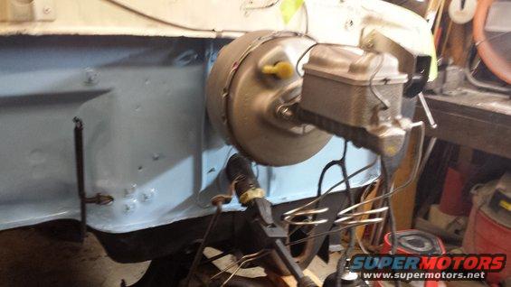 Brake booster and master cylinder assembly mounted on a firewall, with some wiring and plumbing attached