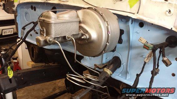 Brake booster and master cylinder assembly in a vehicle's engine bay, with wiring harnesses and brake lines visible
