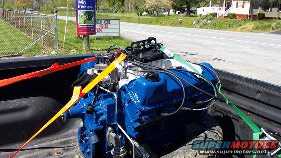Blue engine with yellow and red straps secured in a truck bed