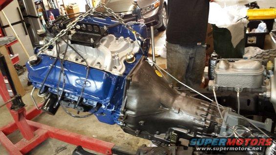 Ford V8 engine with blue valve covers and transmission assembly being lifted by a red engine hoist