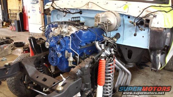 Vehicle chassis with blue engine installed, front suspension visible. Some body panels are off
