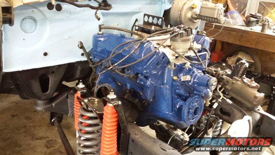 Blue engine block with distributor and wiring, red shock absorbers, and suspension parts in a garage