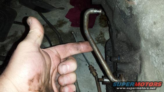 Hand pointing to a metal tube connected to a greasy engine block