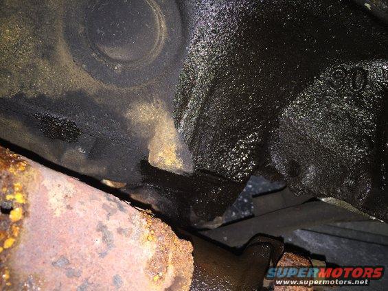 Close-up of oily engine block casting and rusty exhaust pipe