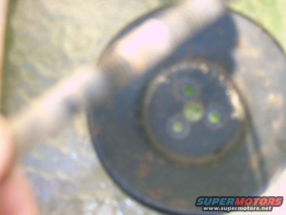 Close-up of a smog pump with green circular openings. Supermotors.net logo at bottom right