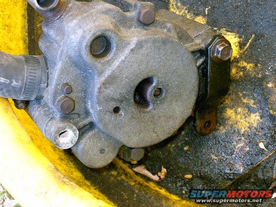 Close-up of a smog pump, likely removed from a vehicle. It's dirty and sits in a yellow container with oil