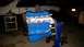 1985 Ford Escort - A blue and silver engine is mounted on a stand, with a white vehicle partially visible behind it.