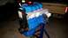 1985 Ford Escort - Engine assembly on a stand, painted blue with a silver intake manifold. A label with text is visible on the black component.