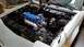 1985 Ford Escort - The engine bay of a car is shown, with a blue valve cover and silver intake pipe.