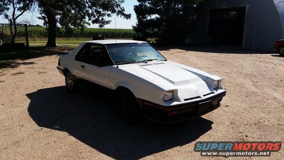 White coupe with a hood scoop parked on a dirt lot