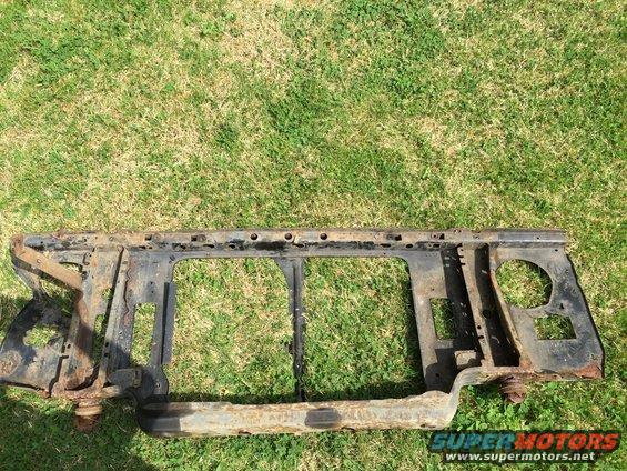 Rusty black metal car radiator support frame with visible rust and damage, lying on grass