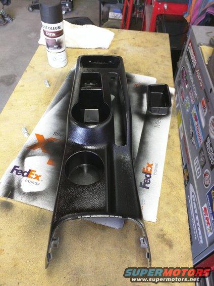 Car center console trim piece with cup holders and storage, next to a can of spray paint