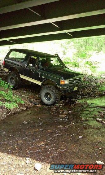 Black Ford Bronco with snorkel and off-road tires driving through a stream